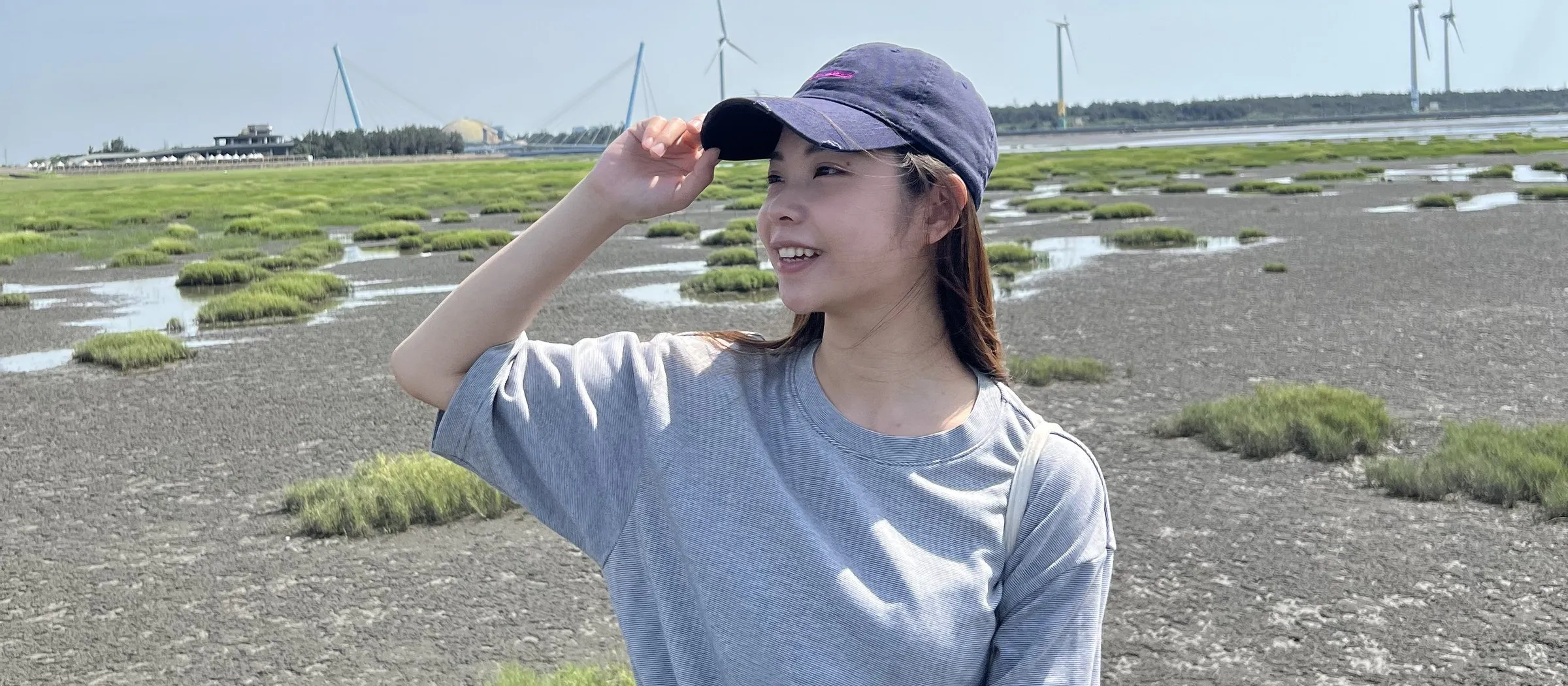 釤釤站在海邊濕地,戴著帽子看向遠方