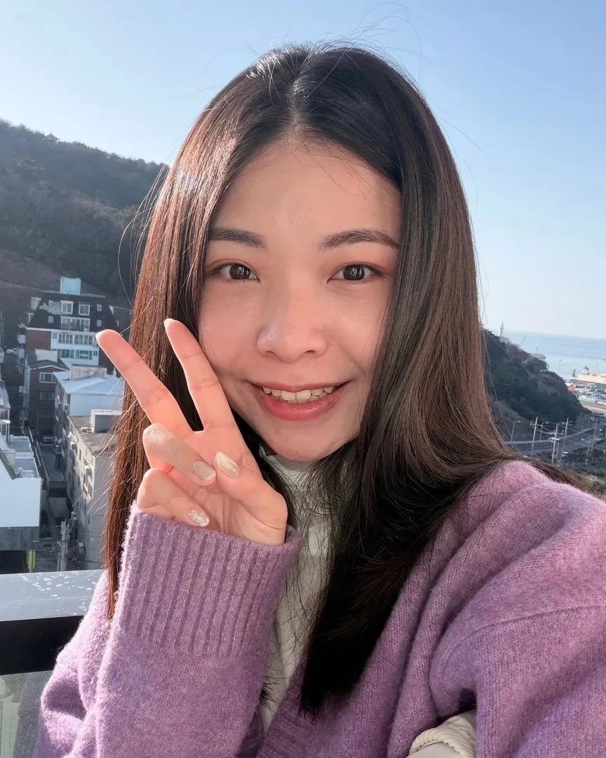 釤釤穿著紫色毛衣，比著 YA 微笑